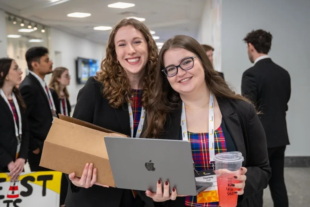 Smiling professionals with laptop and conference badges.