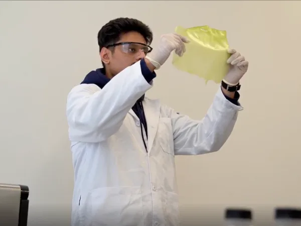 Scientist examines yellow film in lab coat.