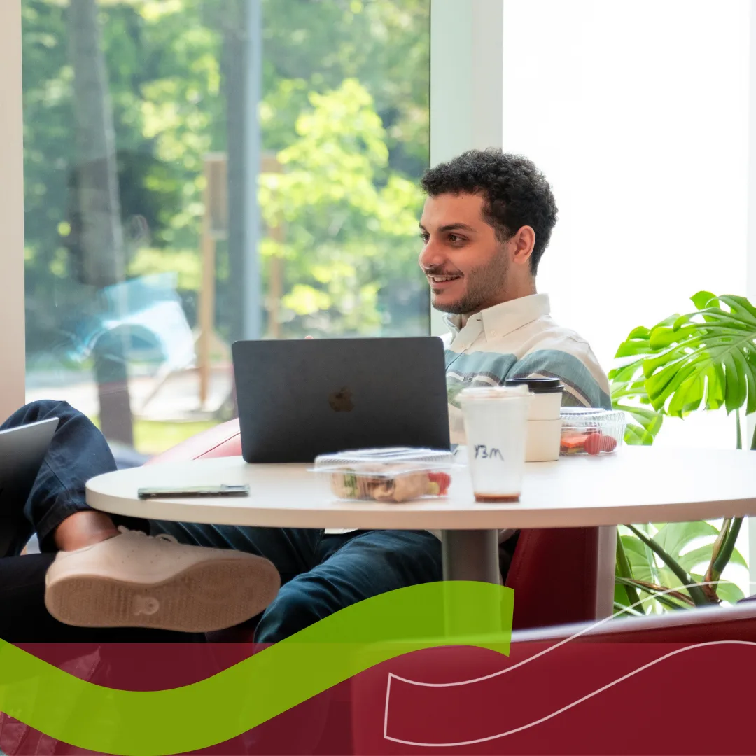 Person working on laptop by a window, smiling.
