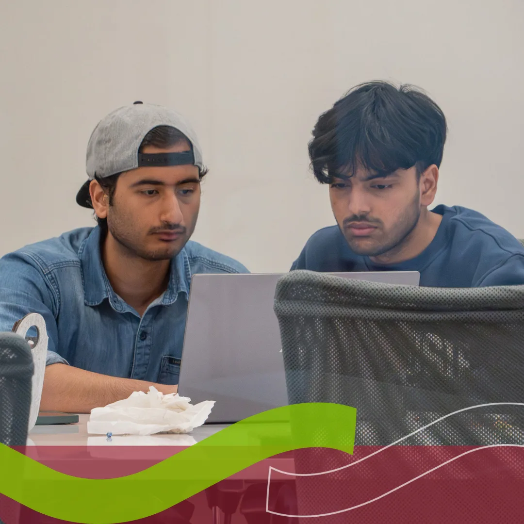 Two men collaborating on laptop at table.
