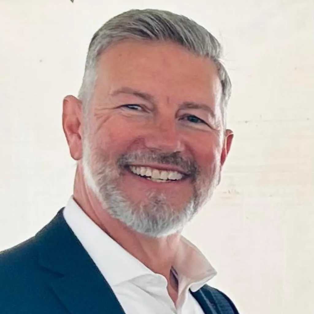 Smiling man in suit with gray hair and beard.
