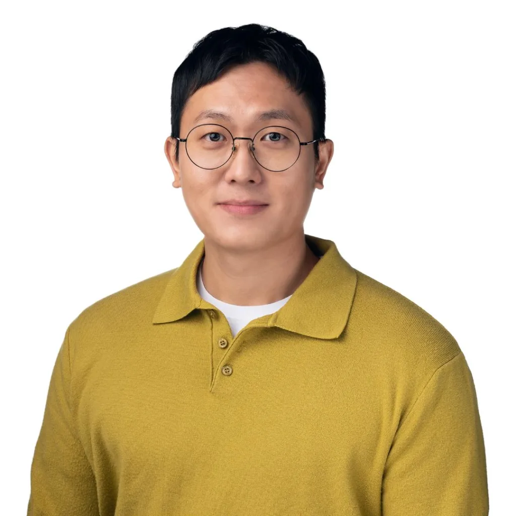 Man in yellow sweater with glasses, smiling.