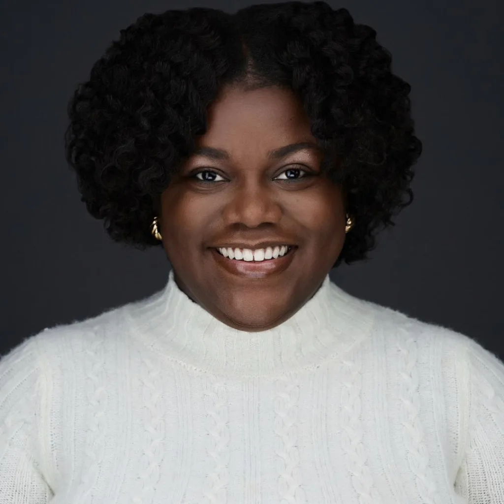 Person smiling in white sweater, dark background.