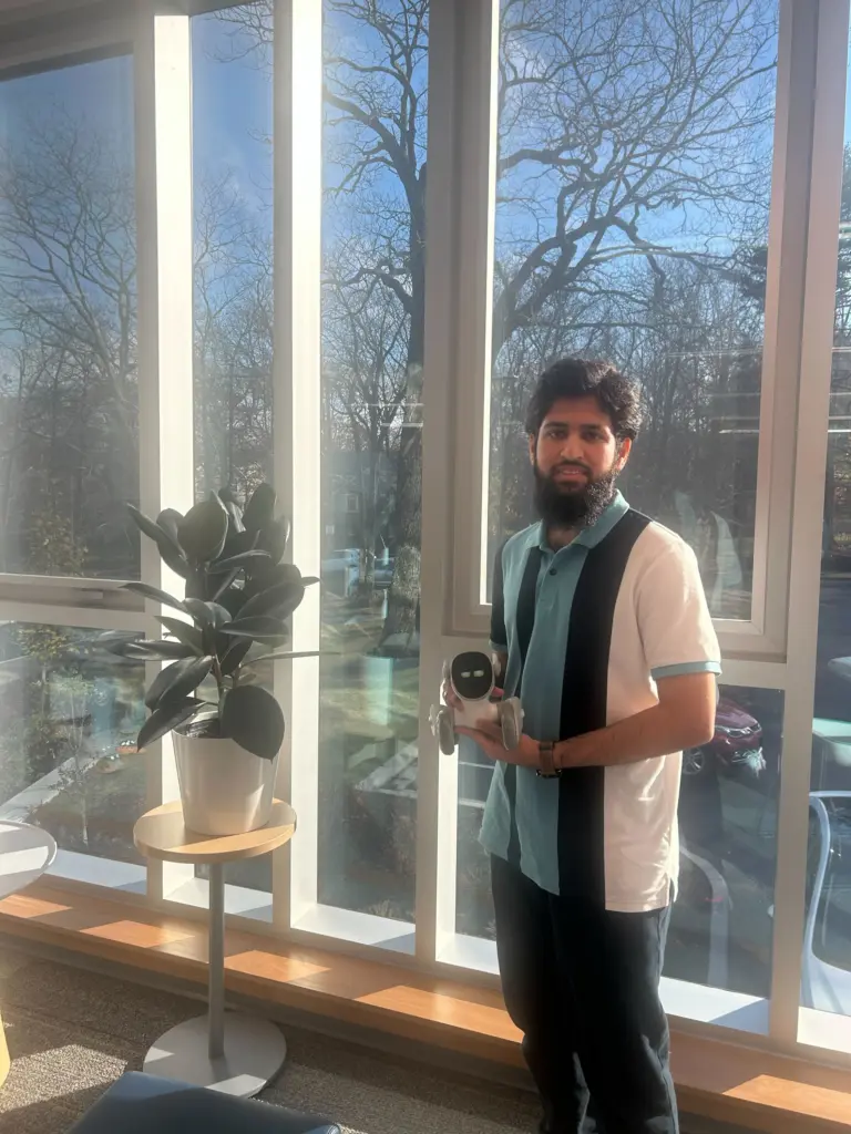 Person holding robot near plant by window.