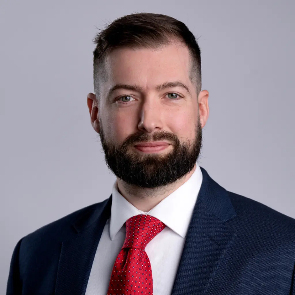 Man in suit and red tie smiling.