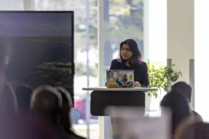 Woman presenting at podium with laptop and screen