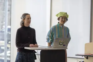 Two women presenting with laptop at podium indoors