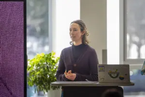 Woman giving presentation beside laptop and display screen