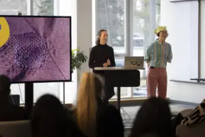 Two presenters discuss textile project beside large screen