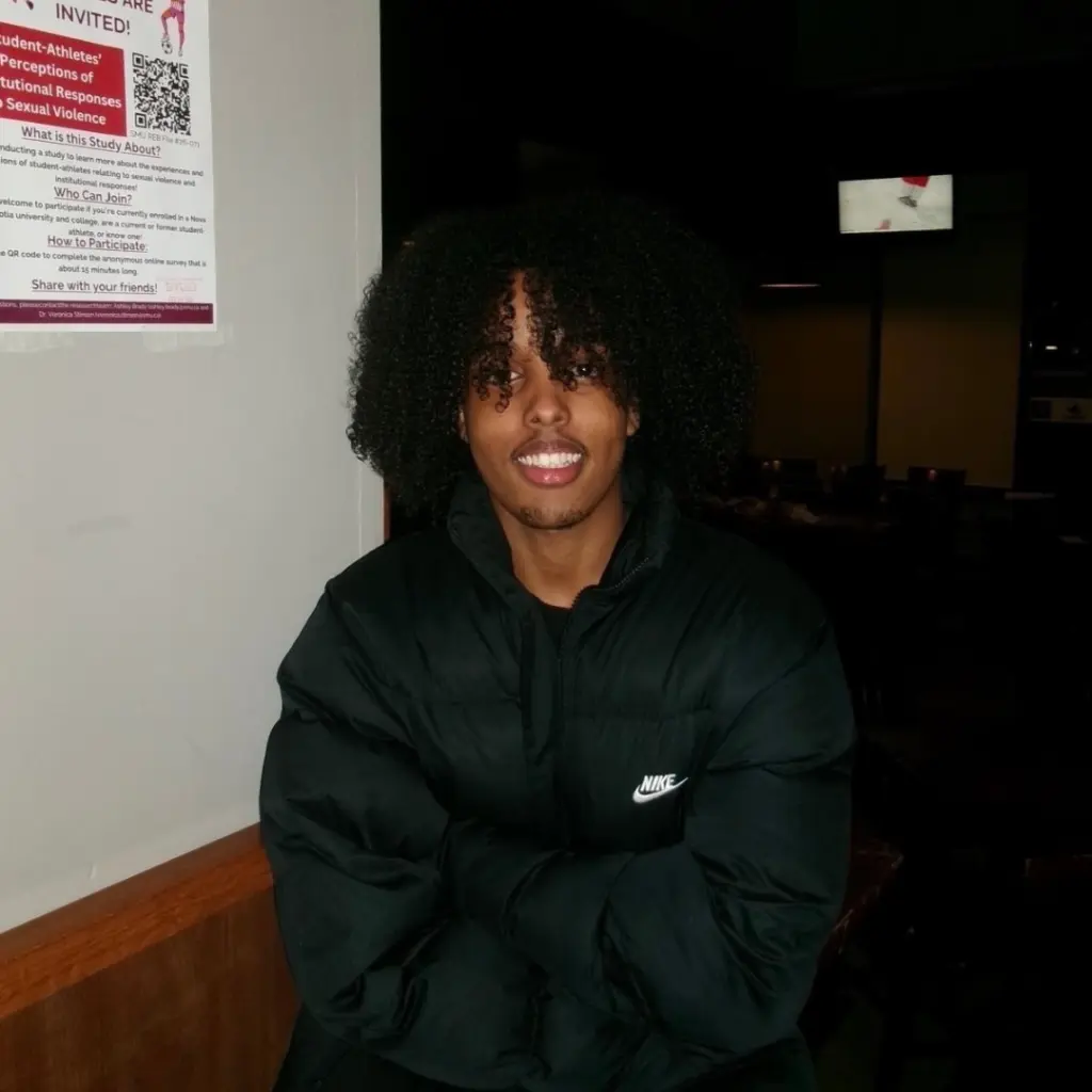 Smiling person with curly hair in black jacket